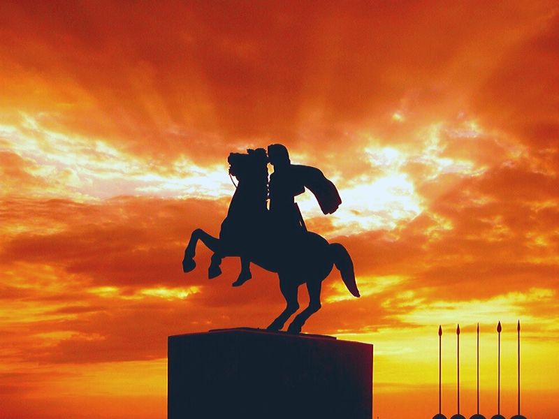 statue of an emperor on a rearing horse silhouetted in front of a colorful sky